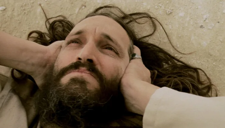 A bearded man lies down protecting his ears in Essential Killing