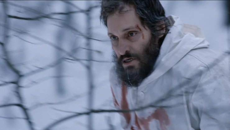 A bearded man in white on the run in the snow in Essential Killing