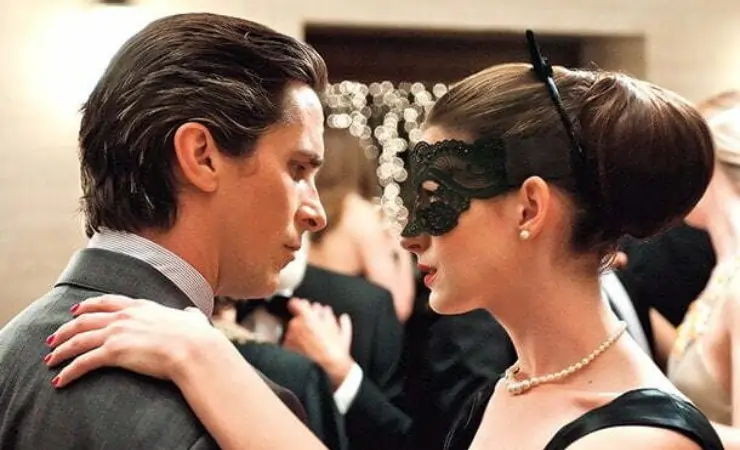 A suited man dances with a dark haired masked woman