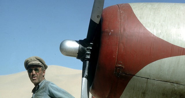 A man dressed like a desert shoulder looks towards an old plane's engine