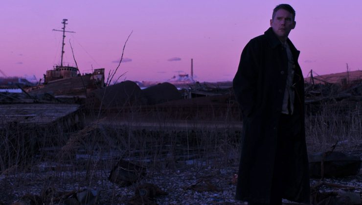 A man of the cloth walks through an industrial area at sunset.