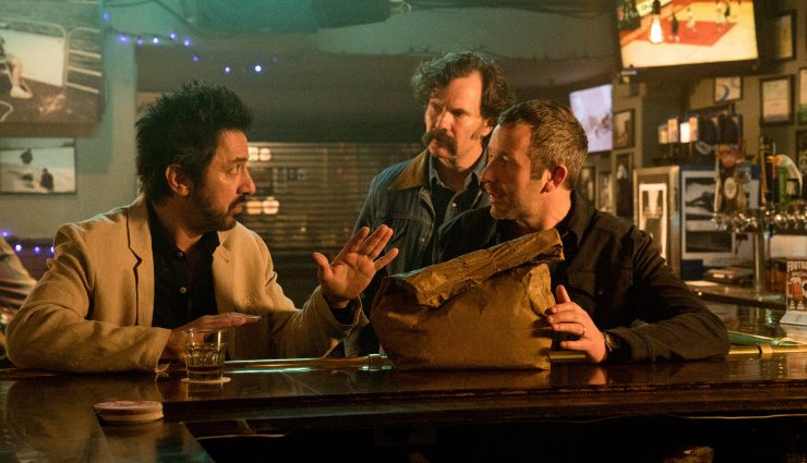 Ray Romano and Chris O'Dowd and another man argue over something in a bag in a bar