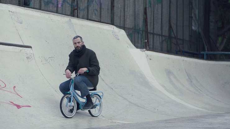 A man rides a child's bike in a skate park in Apples