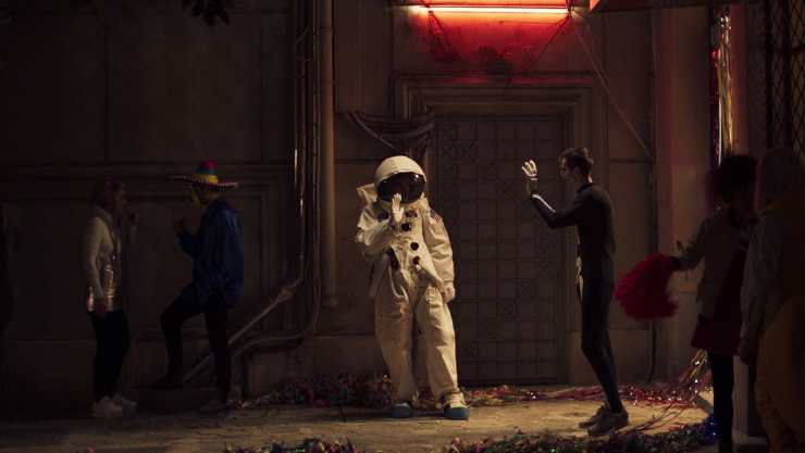 someone in a space suit waves to a man in a darkened room in Apples