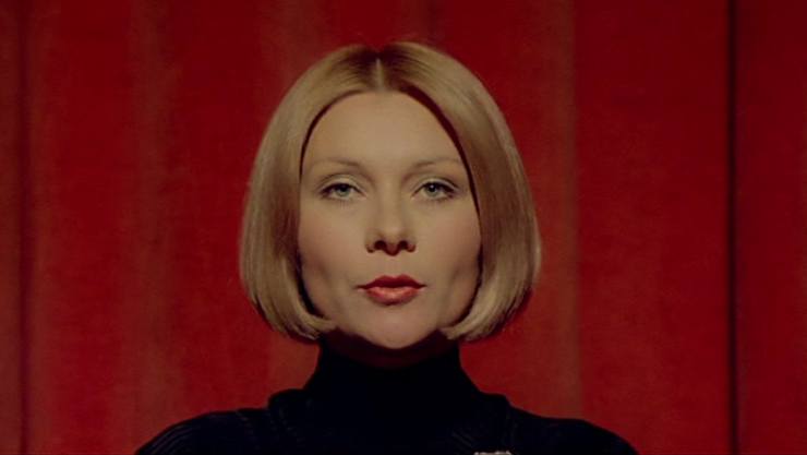 A short haired woman wearing black turtle neck in red background