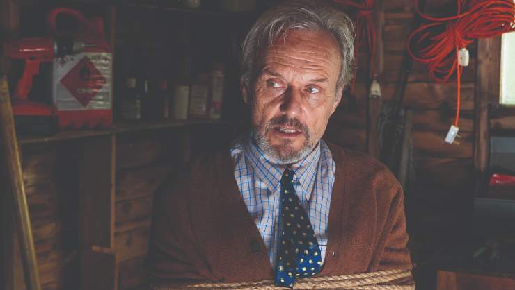 An older man in shirt and tie, is tied down to a seat