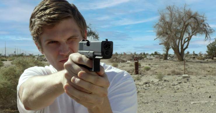 A man with a gun points it at someone in a desert area