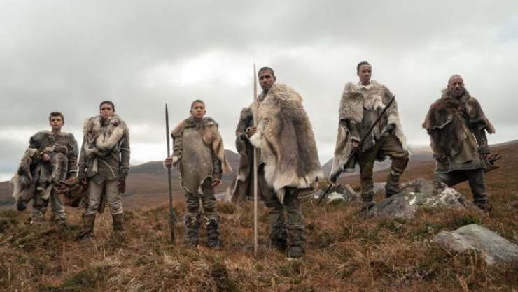 A group of warriors stand in unison wearing furs with weapons.