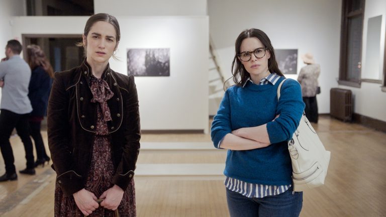 2 women stand looking at a piece of art in a gallery ( The End Of Sex, 2023).