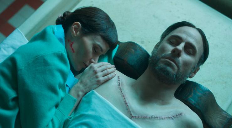 A woman lies next to a dead man