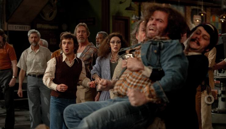 A group of men and women look on as shock as one man is held back angry