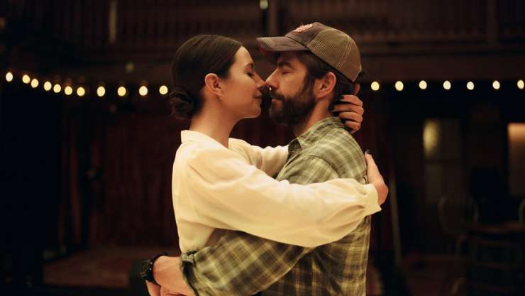 A man with a beard has arms around a dark haired woman about to embrace a kiss