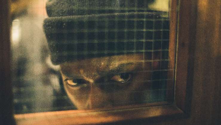 A man hiding behind a door looking into a room in The Group