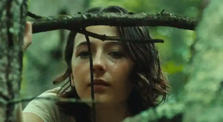 A young woman stands behind the branch of tree