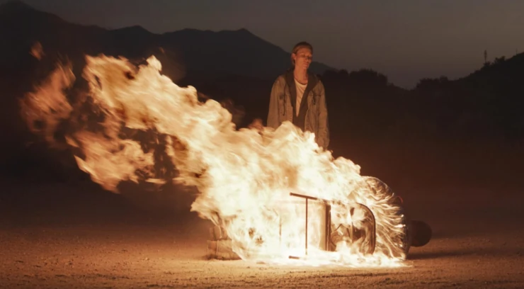 Woman standing over a burning chair in Redux Redux
