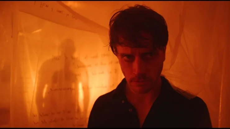 Someone watches a man behind a cover with orange lighting in FrightFest Blockhead