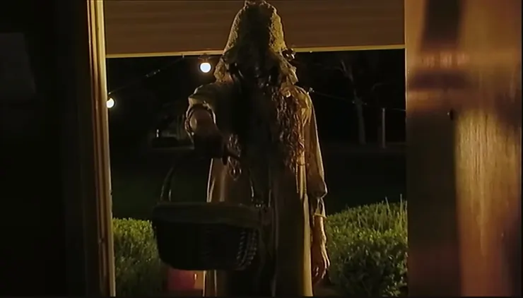 Hooded woman stands at dark doorstep with basket in V/H/S Halloween