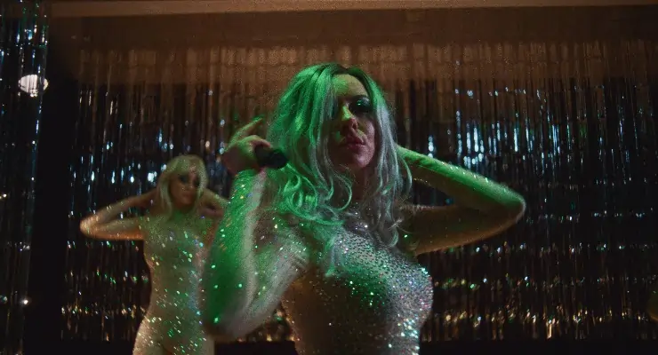 A green haired woman in sparkly dress dances