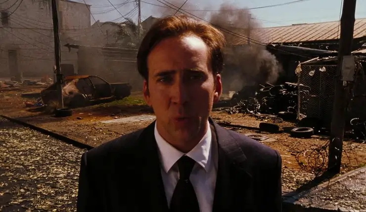A suited man stands in front of a war torn building
