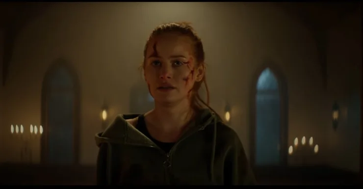 An scarred woman walks through a darkly lit church