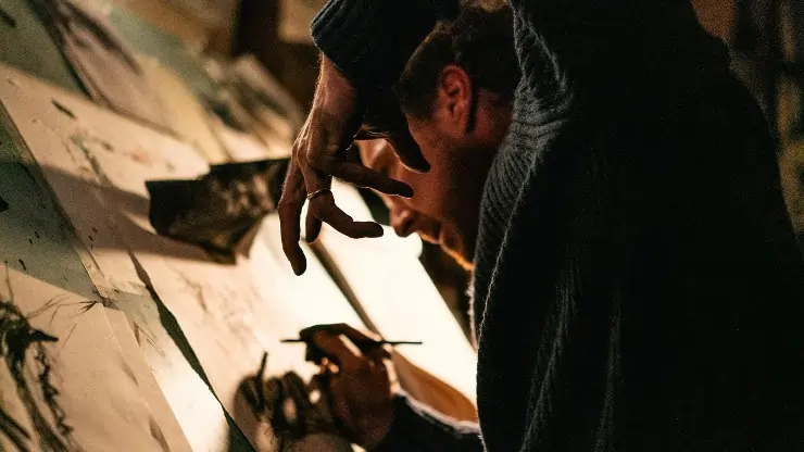 A man at a drawing board attempts to draw something, a crow?