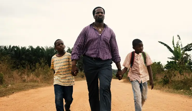 A man walks hand and hand with his 2 sons walking along a dusty road.
