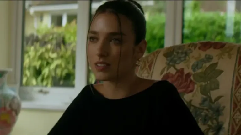 A woman in dark clothing sits looks on in A Gangster's Life (Dua Lipa)
