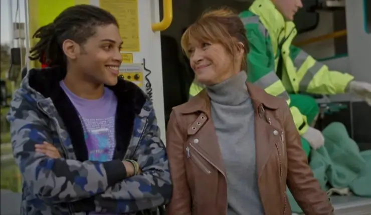 An older woman stands and jokes with a young man next to a ambulance.