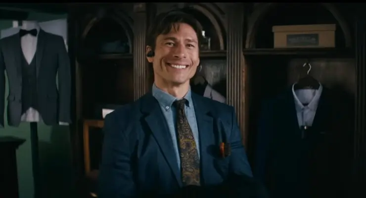 A man in a suit in a suit shop smiles at someone.