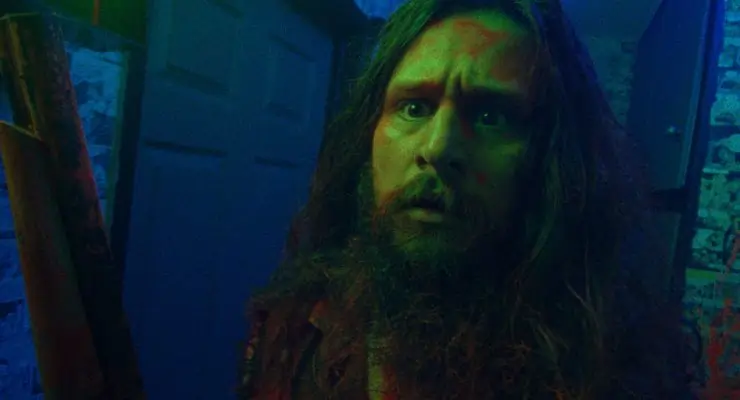 Long haired bearded man with weapon in a neon room in Jimmy and Stiggs.
