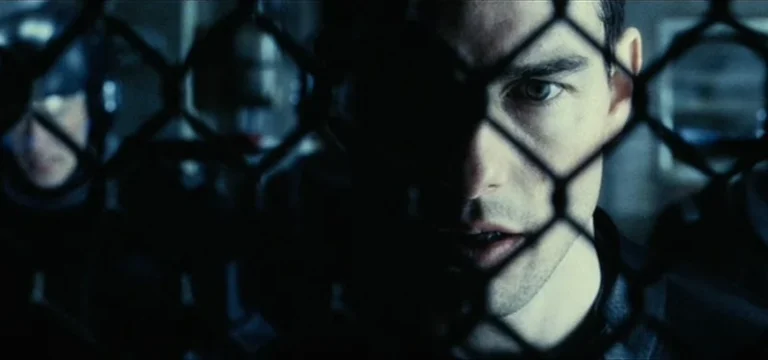 A young Tom Cruise up against a fence with police behind him ready to pounce in Minority Report.