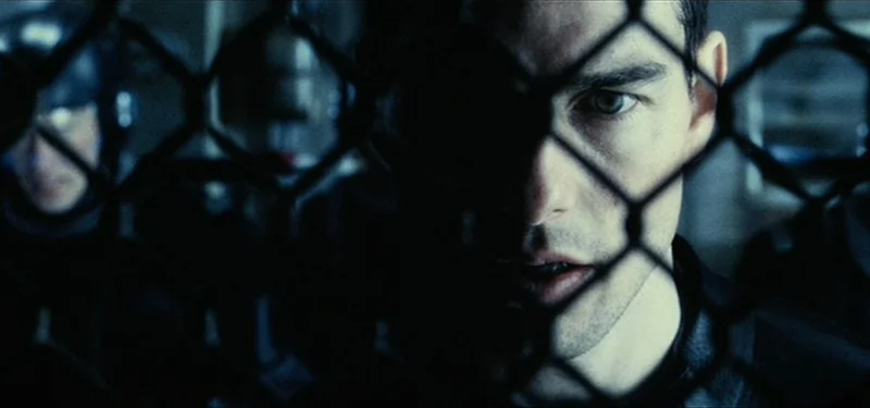 A young Tom Cruise up against a fence with police behind him ready to pounce in Minority Report.