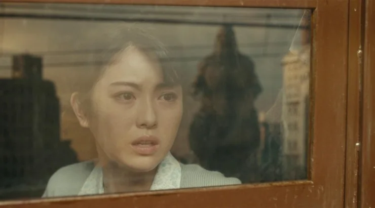 A japanese woman sits in a train in fear in whats approaching in Godzilla Minus One