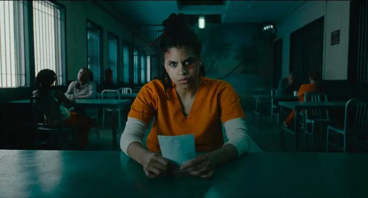 A young angry woman with black eye sits at a desk in a prison in They Will Kill You