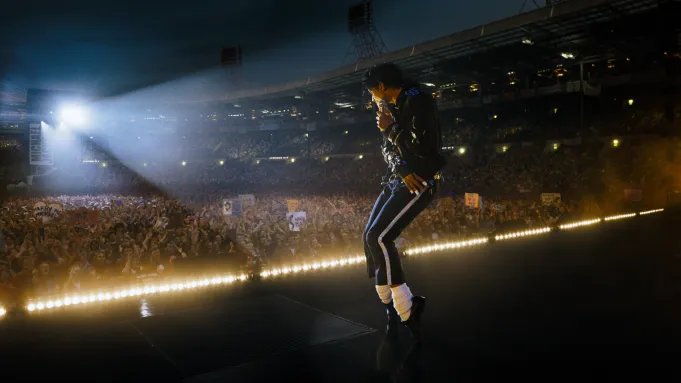Michael peforming a dance move on the stage as thousands of fans watch him in Michael Review