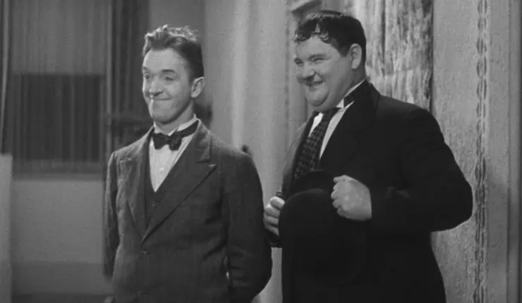Two laughing well suited men share a joke, Laurel & Hardy