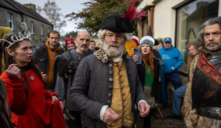 An older r man stands amongst people in period costume
