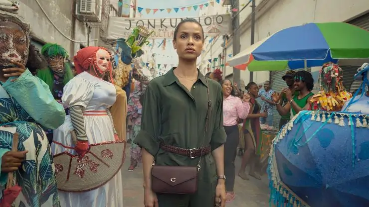 A young bi-racial woman stands in the middle of street surrounded by people in fancy dress or traditional costume in Possession.