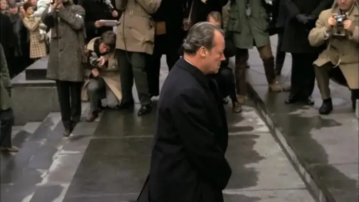 a man in a suit walks past paparazzi
