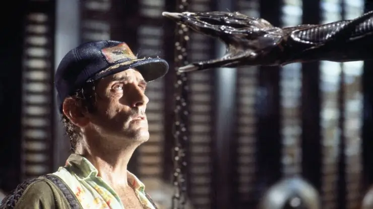 Middle Aged man in a baseball cap looks on in fear as an Alien hand reaches out.