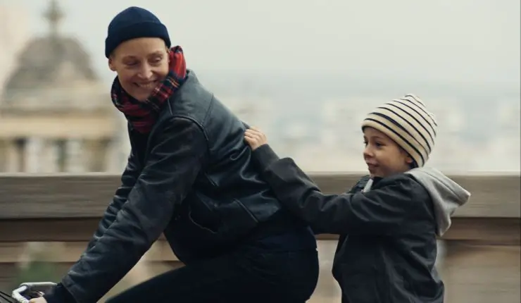 A woman rides a bike with her son on her back in Love Me Tender