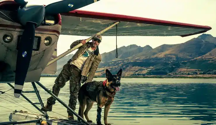 An older man stands on a the edge of a plane on water with his dog.