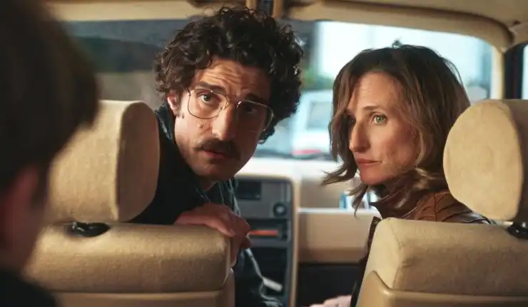 A man in glasses and woman sit in front of car looking around to someone