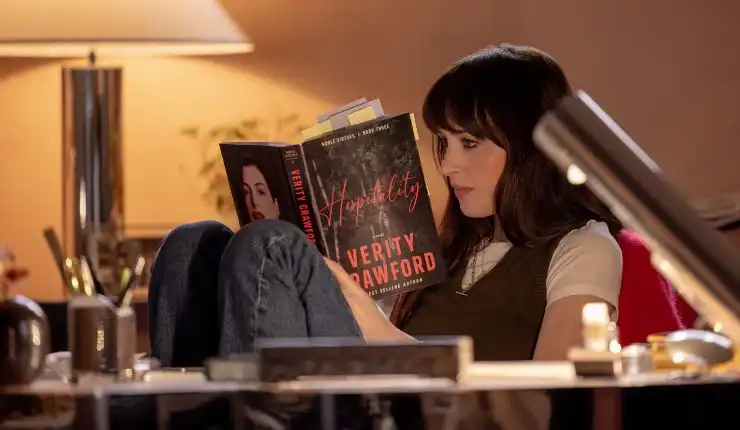 A dark haired woman sits at a desk reading the pages from a book in Verity.