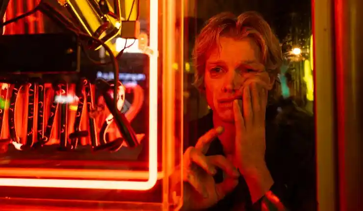 A man with a 'melting' face stands next to a neon sign in Clayface