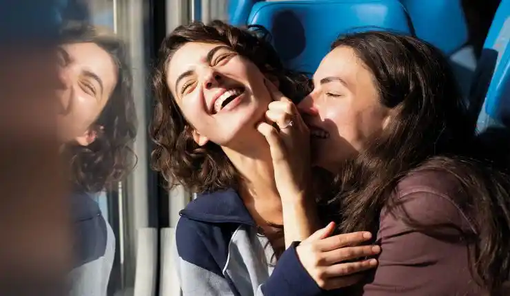 Two young women enjoy a laugh on a train or bus in Idda read review.