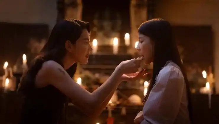 A woman feeds another something in a room full of candles