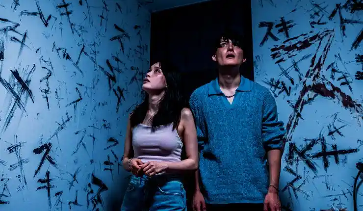 A man and woman walk into a room with marks on the wall in Mag Mag