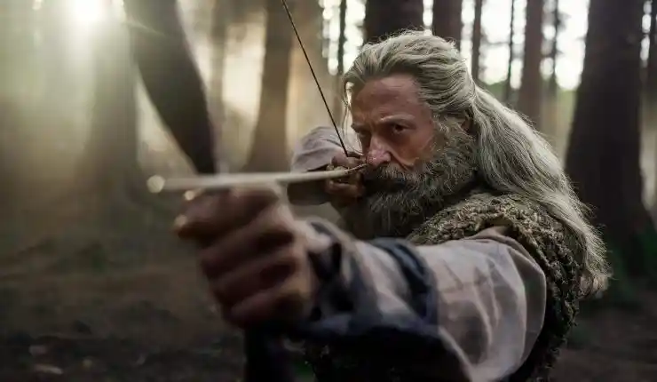 An older bearded man fires a bow and arrow in The Death Of Robin Hood