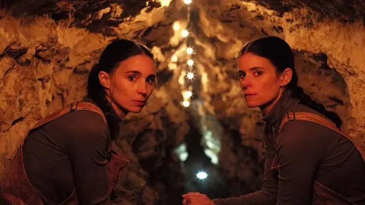 Two woman in a cave stare at the camera